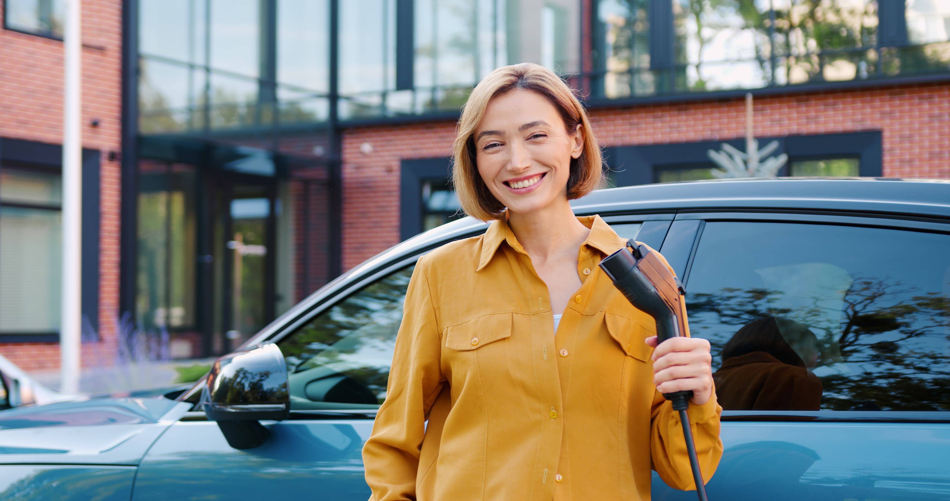 Junge Frau hält Ladestutzen lächeln in die Kamera und will Ihr E-Auto laden
