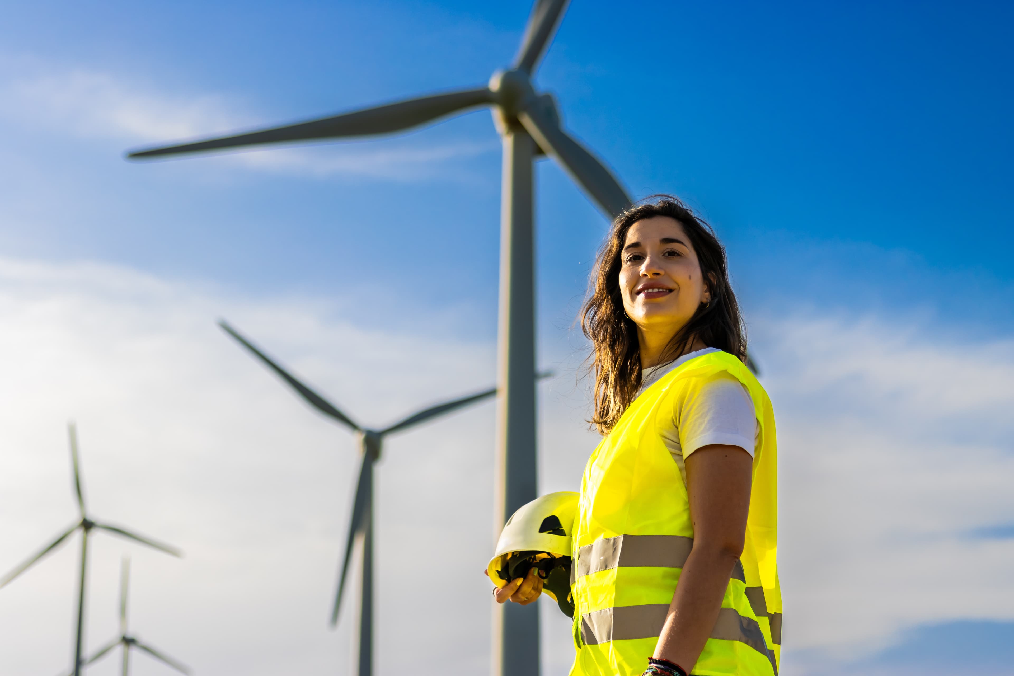 Ingenieurin mit Helm an einem Windpark lächelt in die Kamera mit gelber Warnweste