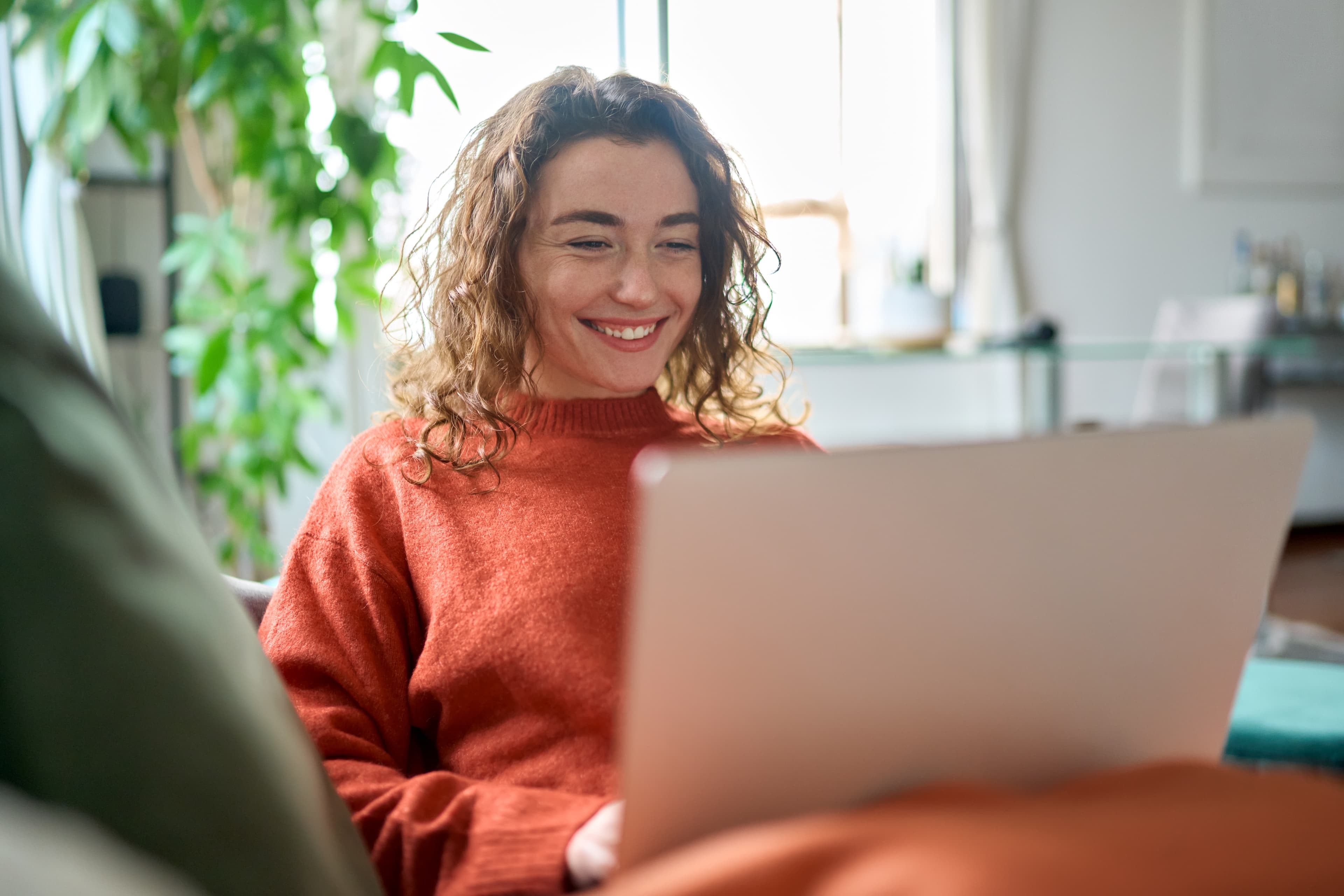 Frau mit Laptop sitze lächelnd auf dem Sofa und schaut auf den Monitor